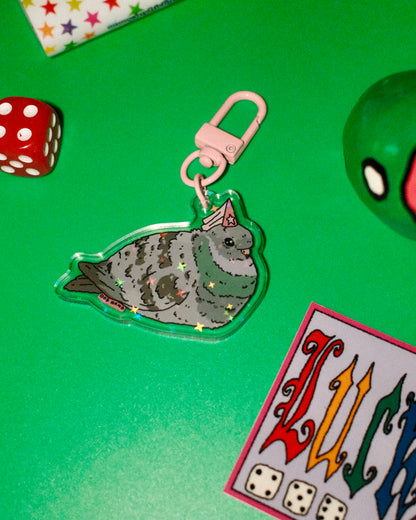 Keychain with a seal design on a green surface with dice and cards.