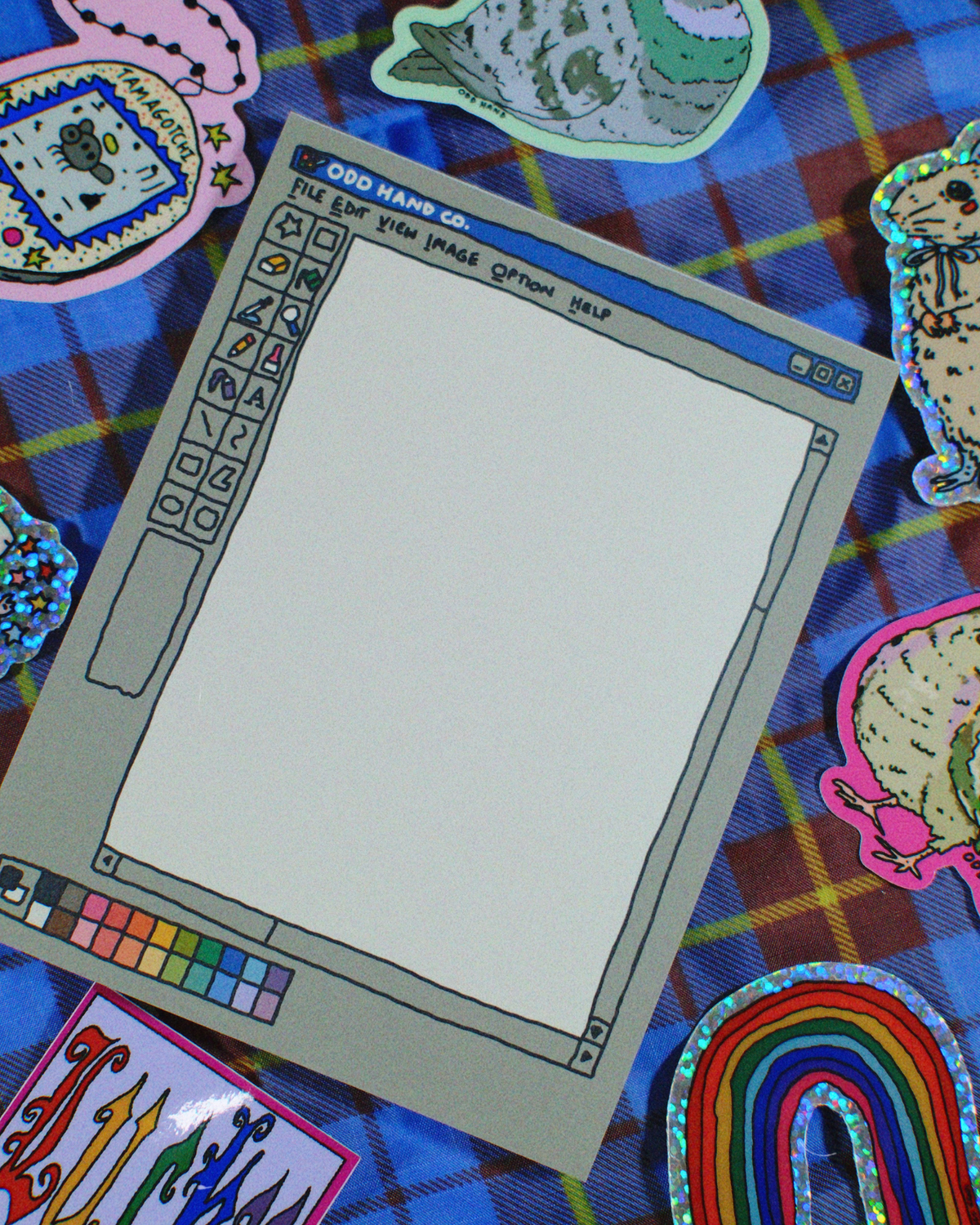 A retro computer-style drawing tablet mockup with a blank white screen, styled on a blue plaid fabric background with colorful cartoon stickers around it.